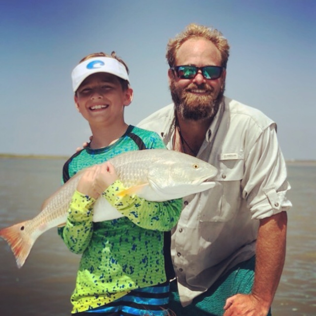 Smiling Captain Ryan with a smiling kid holding a large redfish